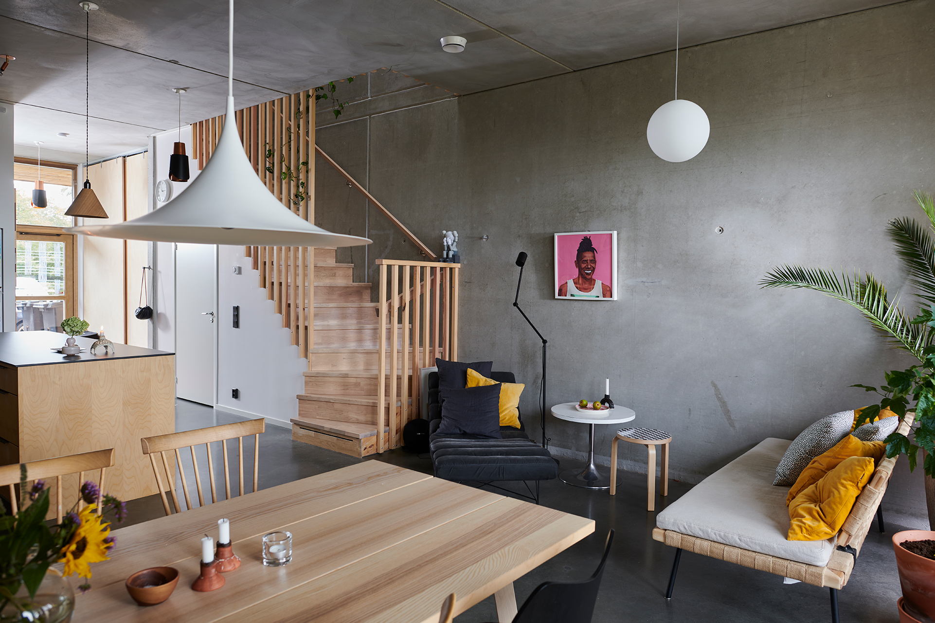 Vardagsrum med betongväggar och trappa i trä till övervåningen